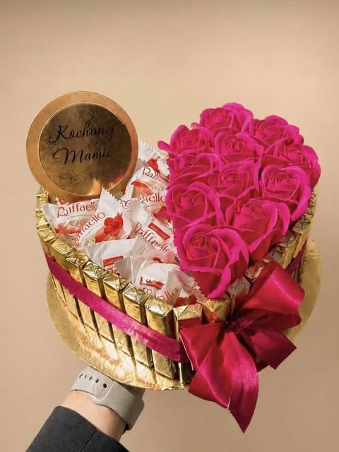 Heart-shaped gift bouquet with vibrant pink roses, chocolates, and wooden personalized plate held in hand against beige background