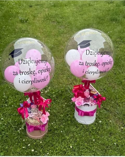 Two pink and white graduation balloon arrangements with thank you messages in Polish, featuring graduation caps and flower bases on green grass.