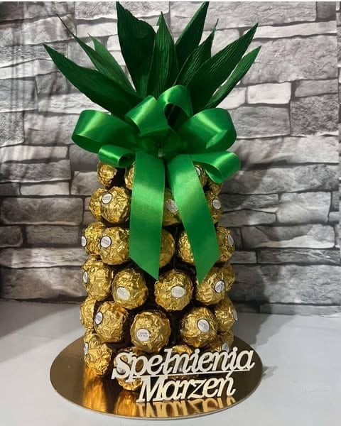 Decorative pineapple made of gold Ferrero Rocher chocolates with green ribbon bow and leaf topper on stand