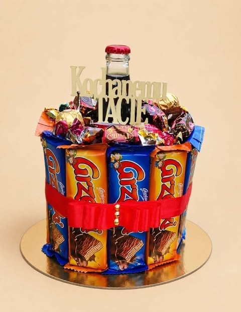 Decorative cake made from stacked colorful snack packages with a red ribbon, topped with candies and a bottle with red cap