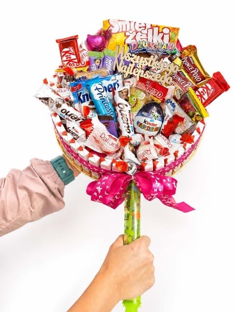 Person holding a candy bouquet with assorted chocolates and sweets arranged in a round bouquet with pink bow