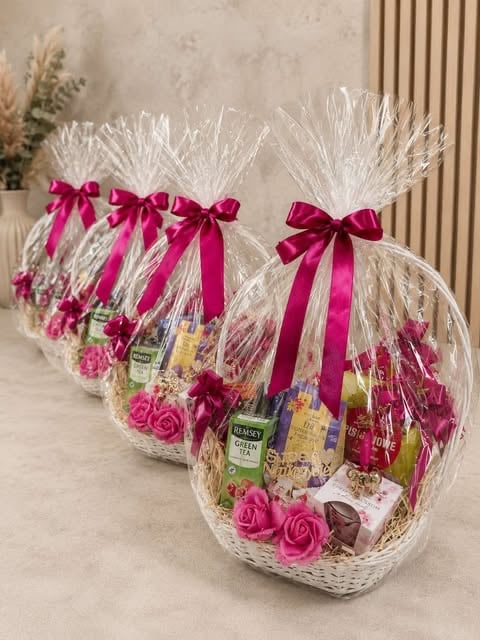 Three gift baskets wrapped in clear cellophane with pink ribbons, filled with spa products, flowers, and bath items on display