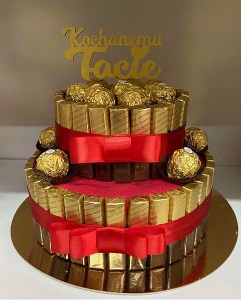 Two-tier golden cake decorated with chocolate candies and red bows, topped with Kachurannu Facta text sign